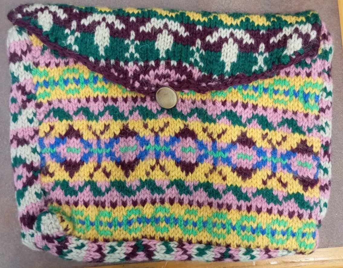Colorful hand-knitted clutch bag with geometric patterns and button closure.