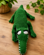 Handmade crochet alligator toy lying on a wooden surface.